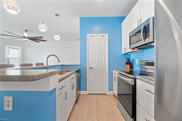 kitchen with pendant lighting, light wood finished floors, stainless steel appliances, white cabinetry, and a sink