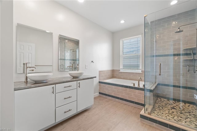 bathroom with a garden tub, wood finished floors, a stall shower, and a sink