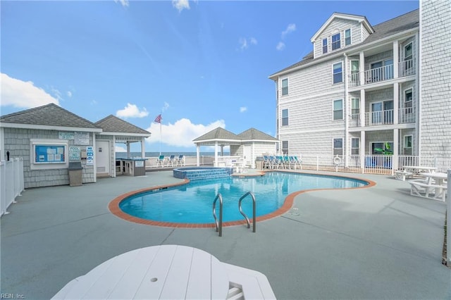 view of swimming pool featuring a water view, a patio area, a pool with connected hot tub, and fence