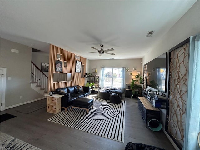 living room featuring baseboards, visible vents, a ceiling fan, dark wood-style flooring, and stairs