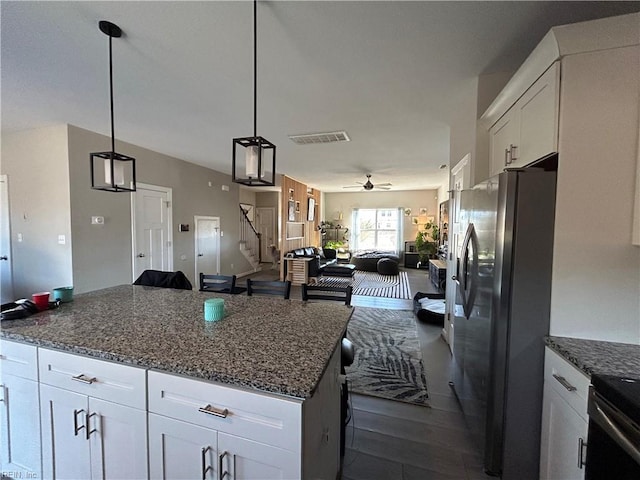 kitchen featuring open floor plan, dark stone countertops, freestanding refrigerator, and white cabinets