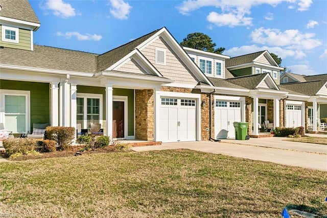 view of front of property featuring stone siding, concrete driveway, roof with shingles, and a front lawn