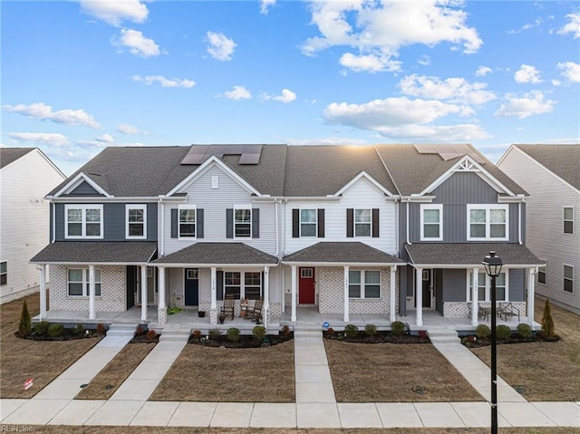 view of property featuring a residential view, covered porch, roof mounted solar panels, and a front lawn