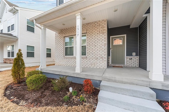 doorway to property featuring covered porch and brick siding