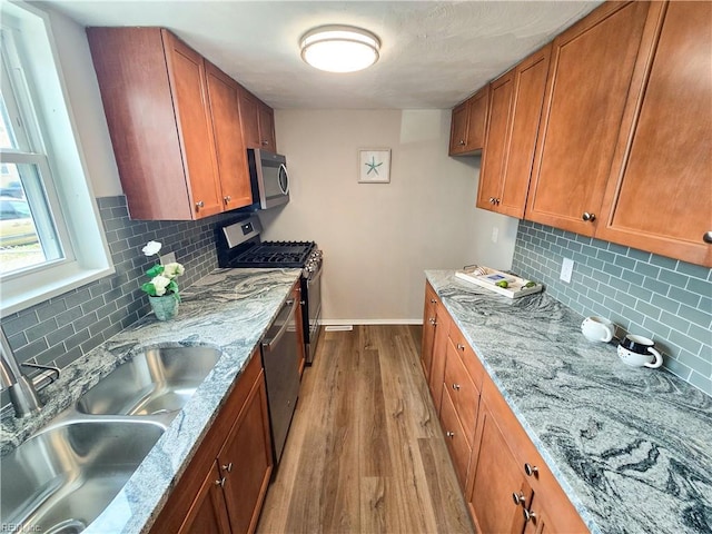 kitchen with a sink, appliances with stainless steel finishes, wood finished floors, and brown cabinets