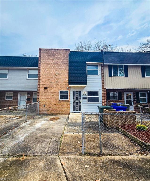 multi unit property featuring brick siding, a fenced front yard, and roof with shingles