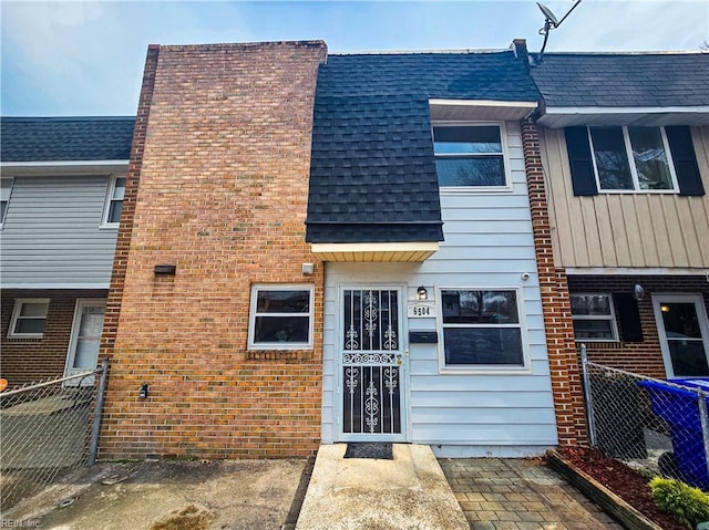 view of front of house featuring roof with shingles, fence, and brick siding