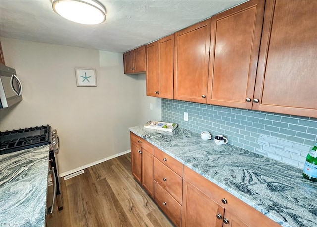 kitchen featuring light stone counters, wood finished floors, baseboards, appliances with stainless steel finishes, and brown cabinets