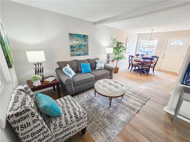 living room featuring an inviting chandelier, beam ceiling, baseboards, and wood finished floors