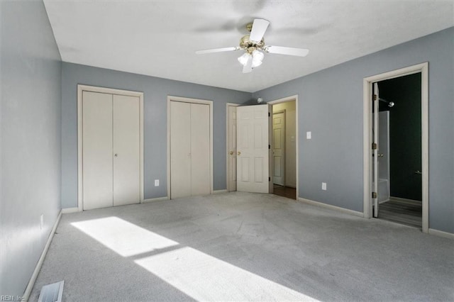 unfurnished bedroom featuring multiple closets, light colored carpet, visible vents, ensuite bathroom, and baseboards