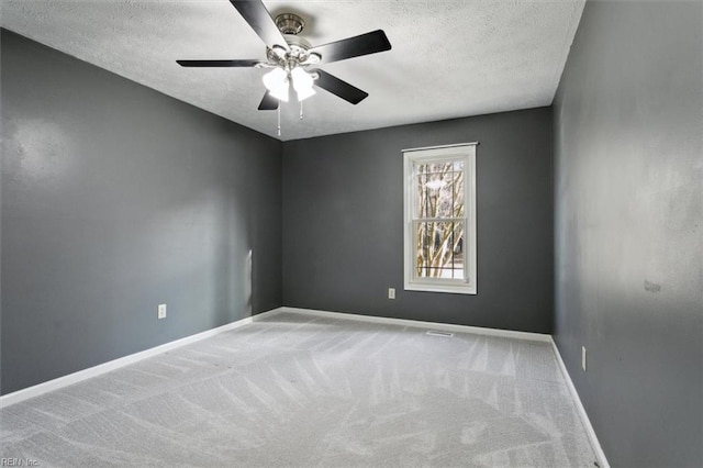 carpeted spare room featuring a textured ceiling, a ceiling fan, and baseboards