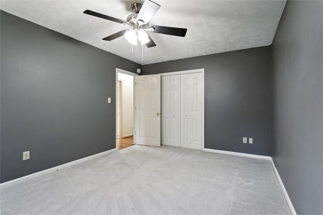 unfurnished bedroom with a closet, light colored carpet, ceiling fan, a textured ceiling, and baseboards