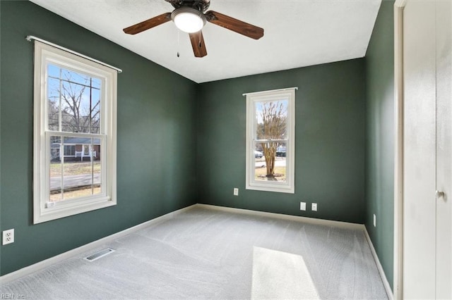 carpeted empty room with baseboards, visible vents, and a ceiling fan