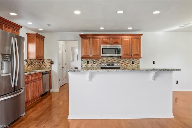 kitchen featuring stainless steel appliances, brown cabinetry, light stone counters, and a kitchen bar