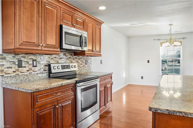 kitchen with light stone counters, stainless steel appliances, backsplash, light wood finished floors, and brown cabinetry