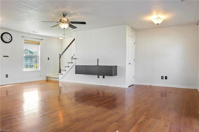 unfurnished living room with stairway, baseboards, and wood finished floors