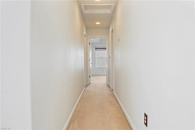 hallway featuring attic access, light carpet, and baseboards