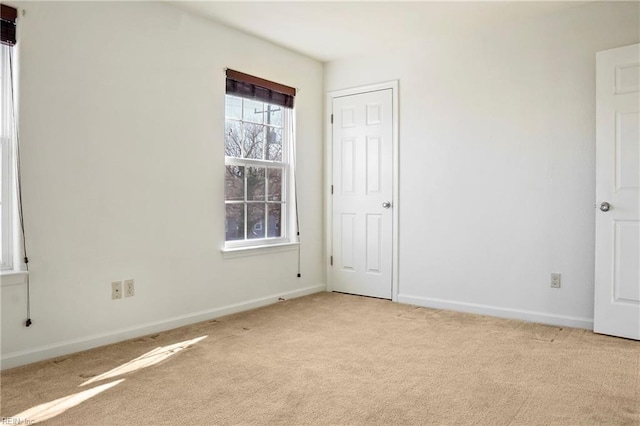 spare room with baseboards and light colored carpet