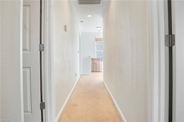 hall with a textured wall, baseboards, visible vents, and light colored carpet