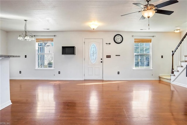 entryway featuring baseboards, stairway, wood finished floors, and ceiling fan with notable chandelier