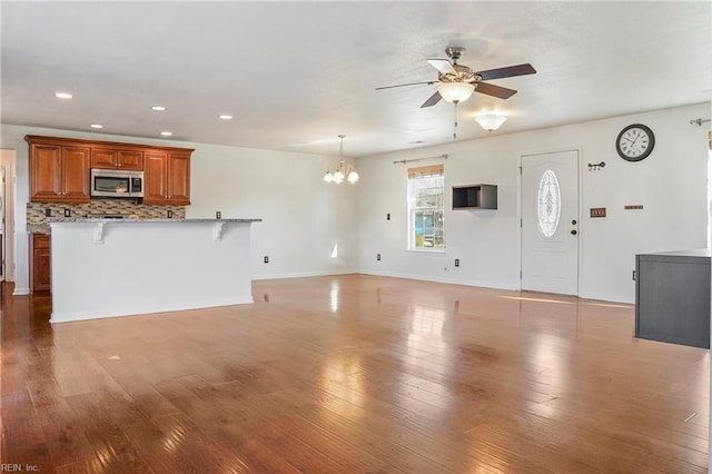 unfurnished living room featuring recessed lighting, baseboards, wood finished floors, and ceiling fan with notable chandelier