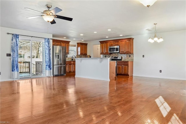 unfurnished living room featuring ceiling fan with notable chandelier, light wood finished floors, baseboards, and recessed lighting