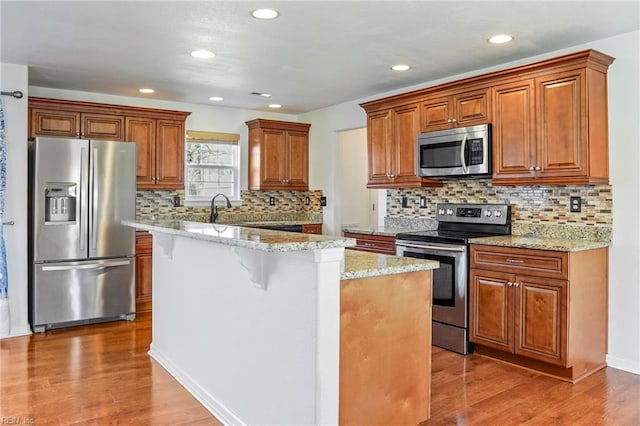 kitchen featuring light stone counters, wood finished floors, a center island, appliances with stainless steel finishes, and brown cabinets