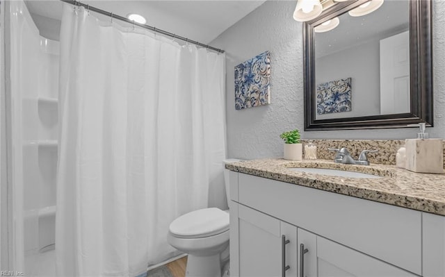 bathroom featuring toilet, a textured wall, wood finished floors, and vanity