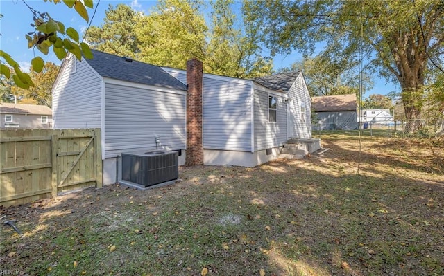 rear view of house with a gate, a chimney, fence, and central AC unit