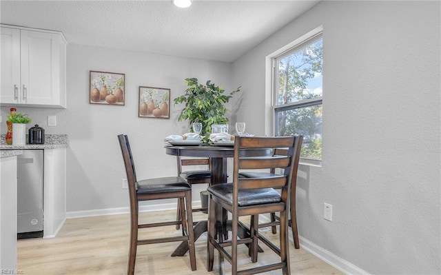 dining space with light wood-style flooring, baseboards, and a textured ceiling