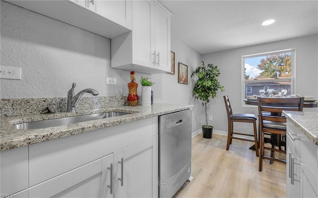 kitchen with light stone counters, stainless steel dishwasher, white cabinetry, a sink, and light wood-type flooring