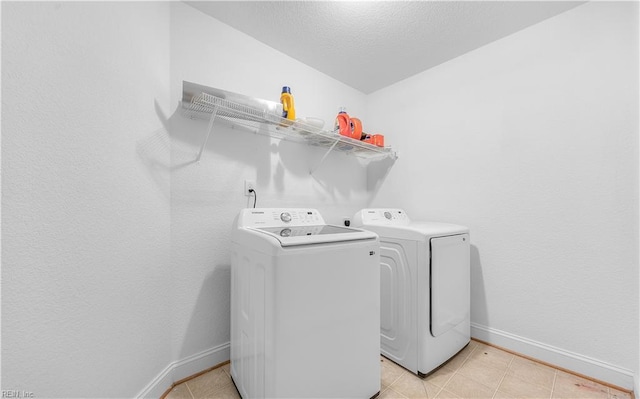 clothes washing area featuring washer and dryer, laundry area, light tile patterned flooring, and baseboards