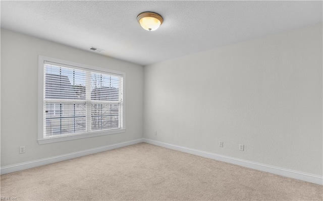 spare room featuring light carpet, visible vents, and a textured ceiling