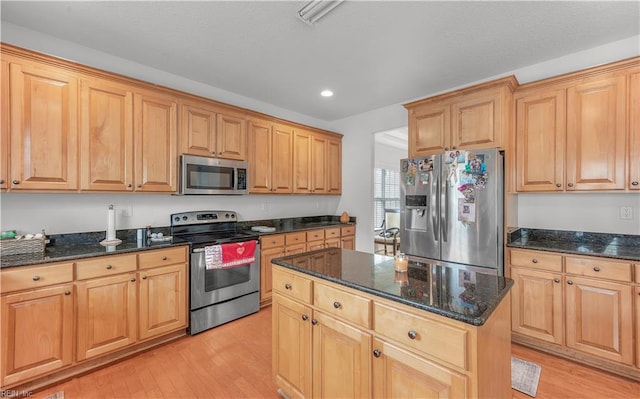 kitchen with light wood-type flooring, dark stone counters, stainless steel appliances, and a center island