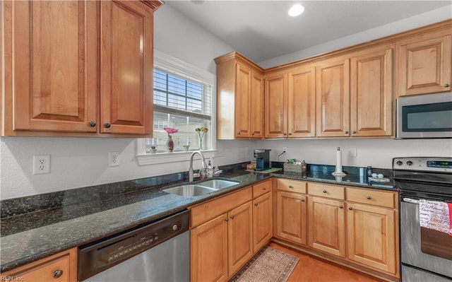 kitchen with light wood-style flooring, appliances with stainless steel finishes, brown cabinetry, a sink, and dark stone countertops