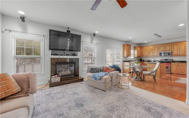 living room featuring light wood-style floors, recessed lighting, visible vents, and a glass covered fireplace