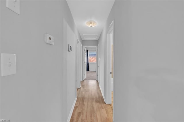 hall featuring attic access, light wood-type flooring, and baseboards