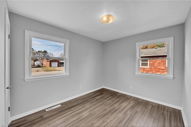 unfurnished room featuring wood finished floors, visible vents, and baseboards