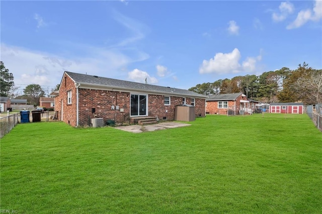 rear view of house with entry steps, a yard, brick siding, and a fenced backyard