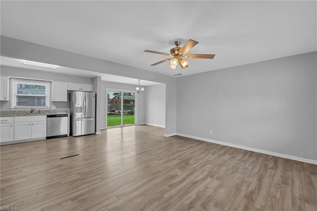 unfurnished living room with light wood-type flooring, a sink, baseboards, and ceiling fan with notable chandelier