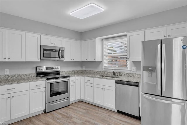 kitchen with stainless steel appliances, light wood finished floors, a sink, and white cabinets