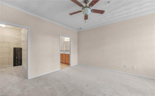 unfurnished bedroom featuring a walk in closet, crown molding, ensuite bathroom, light carpet, and baseboards