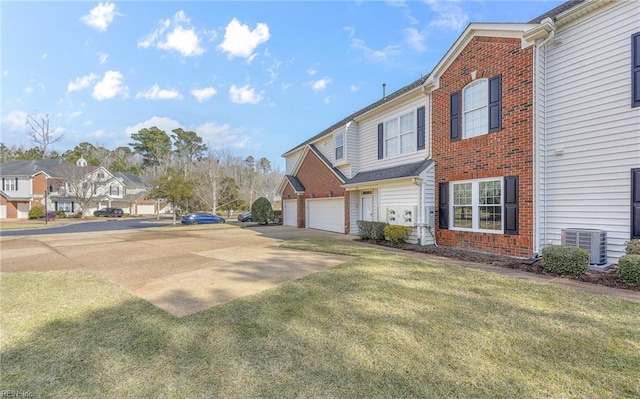 view of side of property featuring driveway, a residential view, cooling unit, a yard, and brick siding