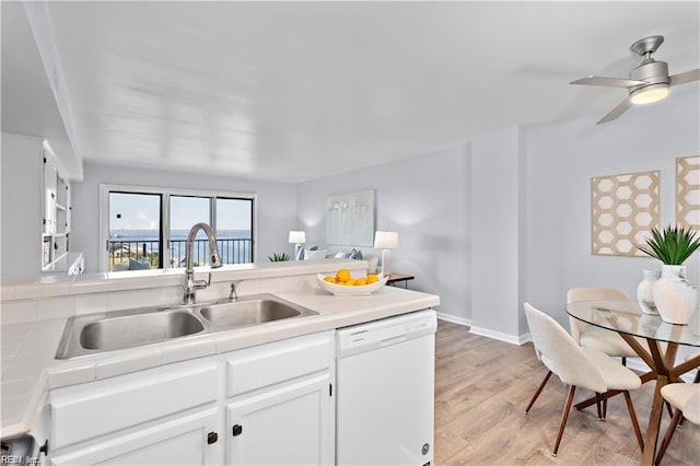 kitchen featuring tile countertops, light wood finished floors, white cabinetry, a sink, and dishwasher