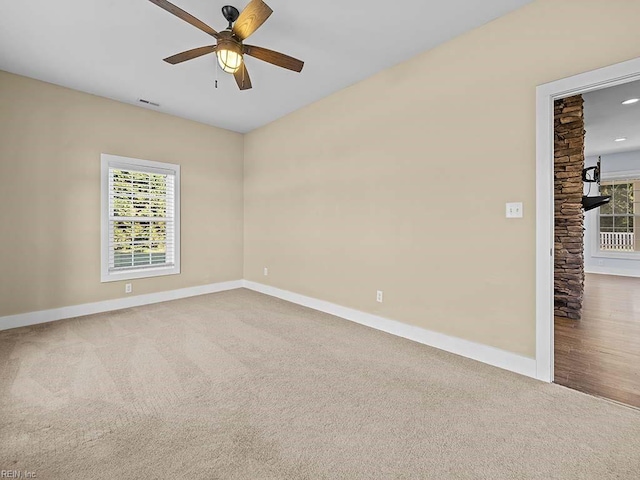 carpeted spare room featuring a wealth of natural light, visible vents, ceiling fan, and baseboards