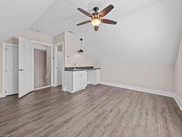 unfurnished living room with a ceiling fan, baseboards, vaulted ceiling, and wood finished floors