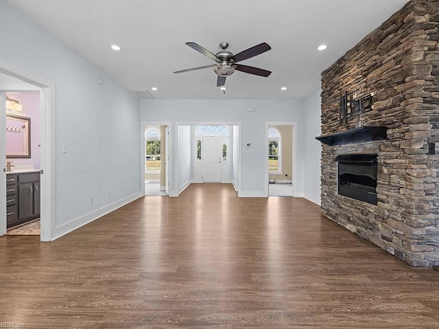 unfurnished living room with a wealth of natural light, a stone fireplace, and wood finished floors