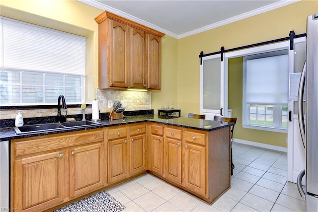 kitchen featuring tasteful backsplash, a barn door, ornamental molding, a sink, and dark stone countertops