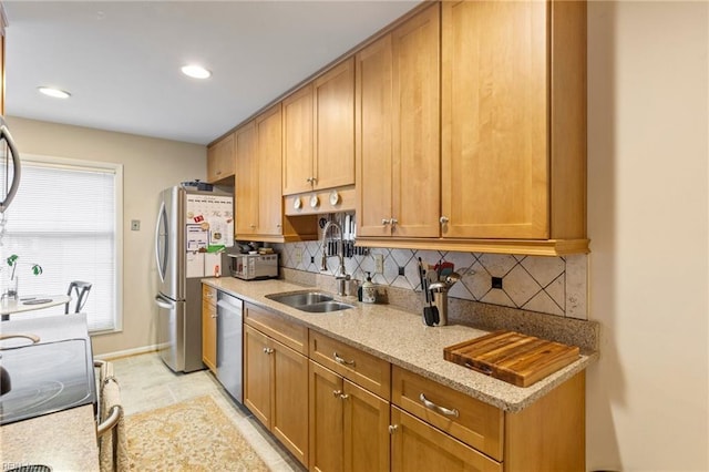 kitchen with baseboards, decorative backsplash, light stone counters, stainless steel appliances, and a sink