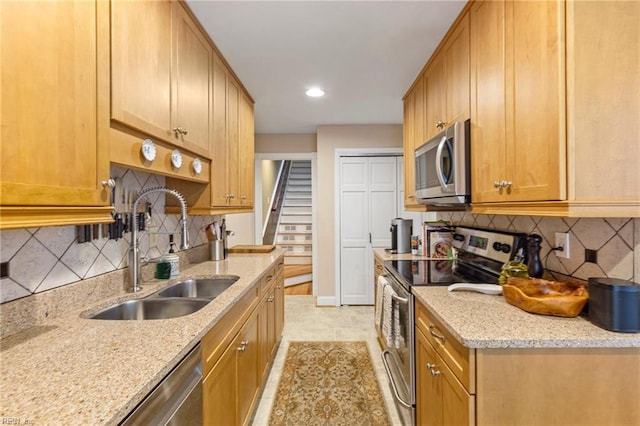 kitchen with light stone countertops, backsplash, stainless steel appliances, and a sink